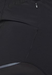 Svart atletiska shorts gjorda av stretchigt material, med en dragkedjeficka, texturerade paneler och kontrasterande meshdetaljer.