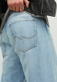 Jeans de mezclilla azul claro con un ajuste holgado, que cuentan con dos bolsillos traseros con costuras curvas y una textura ligeramente deslavada.
