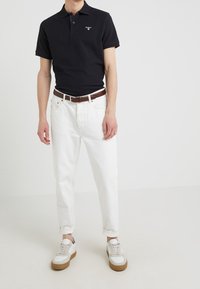 Černé polo tričko, bílé džíny, hnědý kožený opasek a bílé tenisky s hnědými podrážkami. Lesklá bavlna a uvolněný střih.