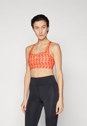 Sports bra in bright orange with yellow leaf patterns, featuring a seamless design and wide shoulder straps. Paired with black high-waisted leggings.