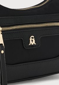 Svart stoffveske med teksturert overflate, med gullglidelås og -beslag, preget logo, og et elegant design.
