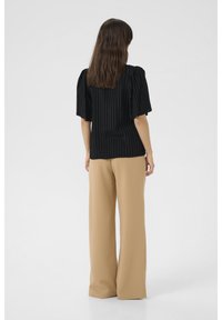 Blusa a righe nere con maniche a sbuffo abbinata a pantaloni larghi beige; tessuto liscio, aderente in vita, con silhouette rilassata.