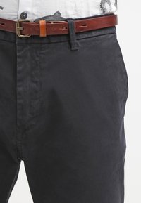 Black cotton trousers with a smooth texture, featuring a brown leather belt and a brass buckle, positioned on a white background.