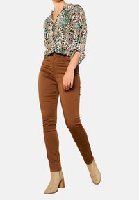 Blusa con stampa animalier verde, beige e nera; pantaloni skinny marroni; stivaletti beige con tacco a blocco. Tessuto liscio, design aderente.