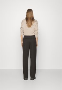 Pull en tricot beige avec un col montant et des poignets roulés, associé à un pantalon noir à jambes larges. Tissu lisse avec une coupe ajustée.