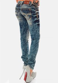 Jeans in denim stone-wash aderenti con tasche posteriori dettagliate indossati con tacchi alti argentati con tacco a stiletto borchiato.