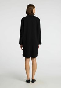 Zwarte jurk met lange mouwen en een kraag, recht model en een knielange zoom. Gladde, uniforme textuur zonder zichtbare patronen of accenten.