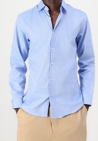 Ljusblå långärmad skjorta i mjukt tyg. Har en knapp-down krage, knappstängning fram och sidoklipp för bättre rörlighet.