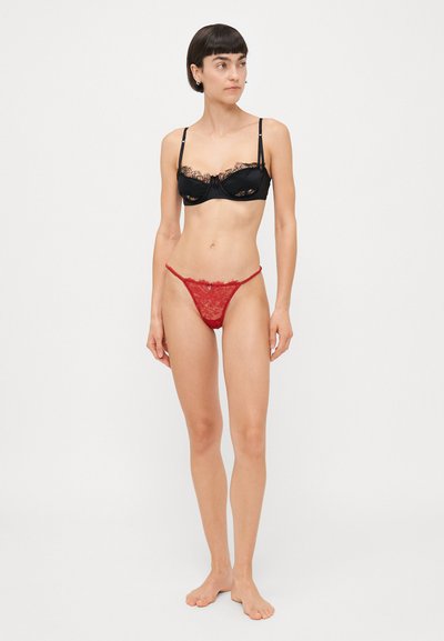 Black lace bra with adjustable straps, featuring a bow detail. Red lace thong with scalloped edges and central embellishment.