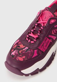 Purple sneakers featuring floral print, leather panels, pink laces, and a chunky white sole. Brand logo on the tongue. Textured details throughout.