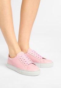 Růžové kožené tenisky s kulatou špičkou, plochou bílou gumovou podrážkou a odpovídajícími tkaničkami. Boční panely mají jemné prošívané detaily.