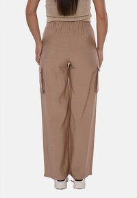 Pantaloni larghi color marrone chiaro con vita elastica, dotati di tasche cargo laterali e una texture liscia, abbinati a sneakers bianche.