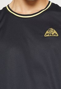 Schwarzes Mesh-Sportshirt mit Rundhalsausschnitt, ausgestattet mit einem schwarz-gelben gestreiften Kragen. Fila-Logo in Gold auf der linken Seite.