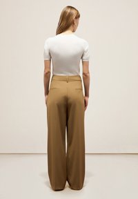 Top corto bianco a maniche corte abbinato a pantaloni marroni a vita alta e di taglio morbido. Tessuto liscio con due tasche posteriori.