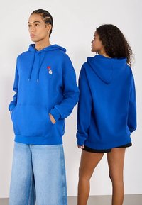 Μπλε φαρδιά φούτερ με μπροστινή τσέπη και κουκούλα με κορδόνι, με μικρό κεντητό σχέδιο στο στήθος. Μαλακό, λείο ύφασμα.