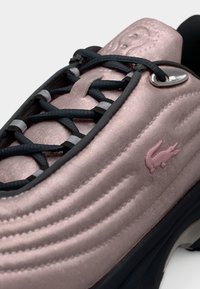 Ροζ σουέντ αθλητικό παπούτσι με σχεδιασμό καπιτονέ, μαύρα κορδόνια, ασημένιες μεταλλικές λεπτομέρειες και ροζ λογότυπο κροκόδειλου. Υφή με στρογγυλεμένη μύτη.