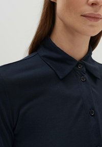 Navy blue collared shirt made of cotton, featuring a smooth texture and button closure, with a fitted design around the neck.