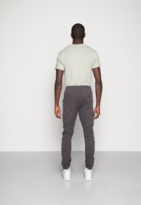 Lichtgrijze T-shirt met korte mouwen, gecombineerd met donkere cargobroek met meerdere zakken en elastische boorden. Witte sneakers maken de look compleet.