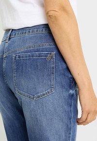 Vaqueros de mezclilla azul con cintura de tiro medio. Incluyen un bolsillo trasero con costuras decorativas y un ligero estiramiento para mayor comodidad.