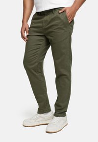 Chinos en coton vert à coupe droite, dotés de poches latérales et d'une texture lisse, associés à des baskets blanches.