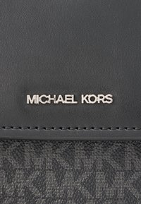 Μαύρο δερμάτινο πορτοφόλι με υφή, ασημένιο λογότυπο «MICHAEL KORS» και διακριτικές ραφές κατά μήκος της άκρης.