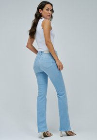 Los jeans acampanados de color azul claro presentan una cintura de altura media, cinco bolsillos y un ligero desvanecimiento. Se llevan con una blusa sin mangas blanca y sandalias de tacón.