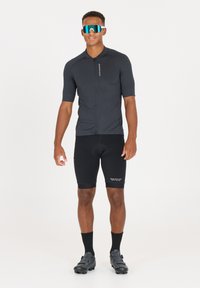 Kurzärmliges Fahrradjahr in Dunkelgrau, mit einem Reißverschluss auf der Vorderseite und dezentem Branding, kombiniert mit schwarzen gepolsterten Shorts und schwarzen Fahrradschuhen.