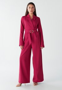 Fuchsia wijde jumpsuit met lange mouwen, een ceintuur in de taille en een notched lapel. Glad materiaal met een aansluitende top en een relaxte pasvorm door het geheel.