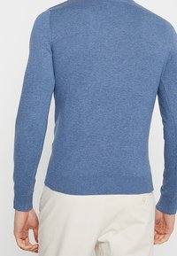 Niebieski sweter dziany o dopasowanym kroju, z długimi rękawami, ściągaczami przy mankietach i u dołu. Wykonany z miękkiego materiału o gładkiej teksturze.