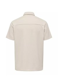 Camisa beige de manga corta con cuello. Presenta un dobladillo recto y una sola costura en el yugo trasero, hecha de una tela suave.