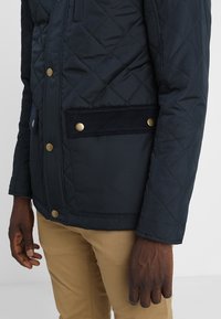 Prošívaná námořnická bunda se sametovým lemem kapes, kovovými knoflíky a úzkým střihem. Měkká textura a viditelný geometrický vzor.