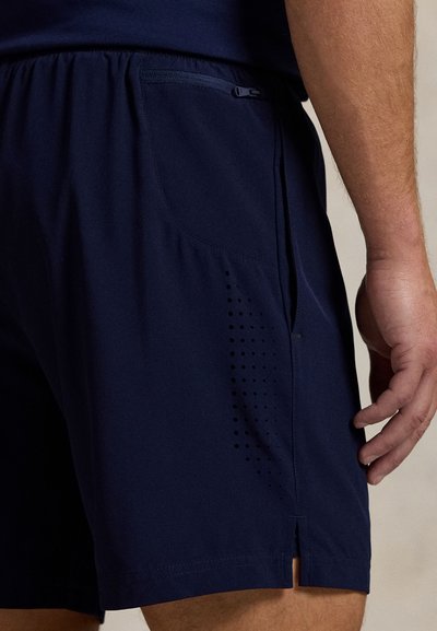Tamsiai mėlyni sporto šortai iš lengvos medžiagos, su skeltu kraštu, šoninėmis kišenėmis ir perforuotomis detalėmis kvėpuojamumui užtikrinti.