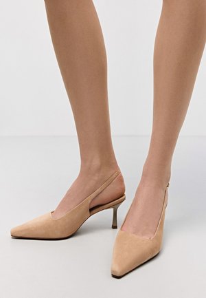 Beżowe zamszowe szpilki typu slingback z wąskim czubkiem, cienkim obcasem i wyciętymi bokami. Gładka tekstura z minimalnymi akcentami.