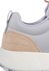 Sneaker met een grijze synthetische bovenkant en een beige suède accent, met textuurstiksels en een witte rubberen zool. Logo is op de zijkant geperst.