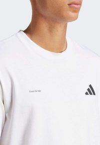 Hvid bomulds T-shirt med et sort Adidas-logo og teksten "Fra logoet" på brystet. Kortærmede og med rund hals.