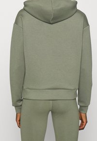 Olivově zelená mikina z bavlněné směsi, s kapucí, spadlými rameny a žebrovaným lemem. Hladká textura a volný střih.