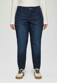 Granatowe dżinsy o slim fit, z kieszeniami z przodu i zapięciem na guziki. W połączeniu z beżowymi i kremowymi trampkami.