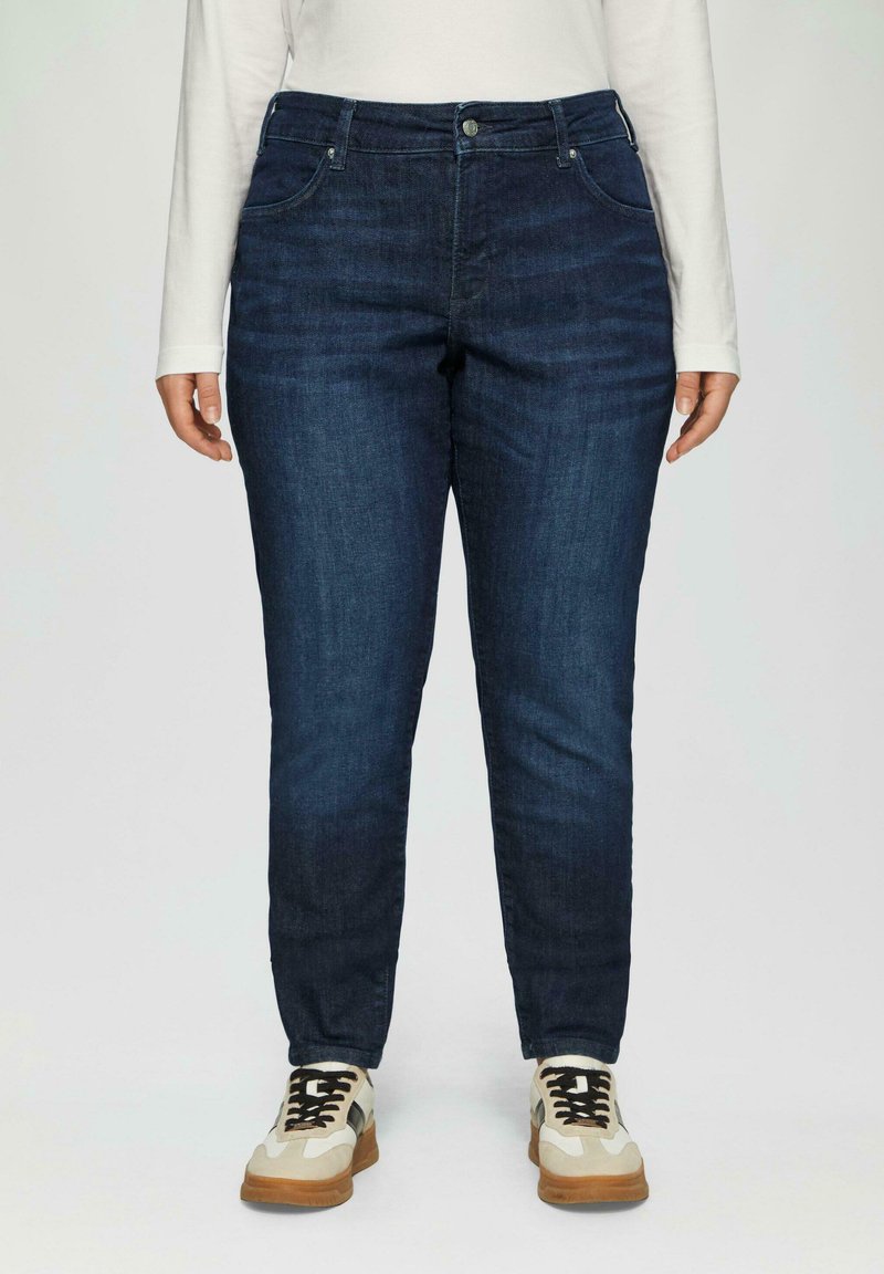 Granatowe dżinsy o slim fit, z kieszeniami z przodu i zapięciem na guziki. W połączeniu z beżowymi i kremowymi trampkami.