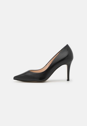 Pompe à talon aiguille en cuir noir avec un bout pointu. Texture lisse, talon aiguille mince, et une semelle intérieure beige visible de profil.