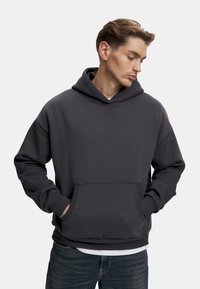 Mörkgrå hoodie i mjukt bomullsblandat material, med ficka fram och ribbad mudd. Diskret logotyp på bröstet, avslappnad passform.