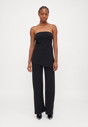 Zwarte strapless top gecombineerd met wijde zwarte broek, gemaakt van gladde stof, met een diagonale zoom en stijlvolle zwarte pumps met puntige neuzen.