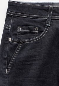 Jeans de mezclilla oscura con corte ajustado, costuras claras en contraste y un bolsillo frontal con un detalle de remache metálico.