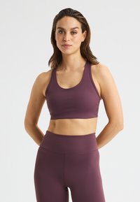 Lila Sport-BH mit runder Ausschnittform und breiten Trägern, gefertigt aus glattem, dehnbarem Material, kombiniert mit passenden, hochgeschnittenen Leggings.