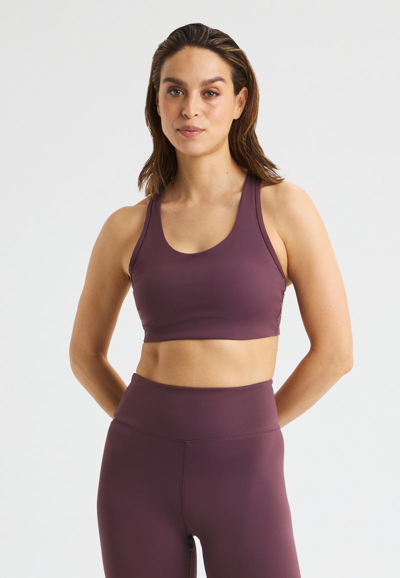 Lila Sport-BH mit runder Ausschnittform und breiten Trägern, gefertigt aus glattem, dehnbarem Material, kombiniert mit passenden, hochgeschnittenen Leggings.