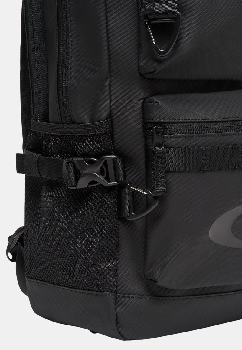 Coin de sac à dos noir avec poche latérale en mesh, sangle réglable avec boucle à dégagement rapide, petite poche avant zippée et clip en D métallique.