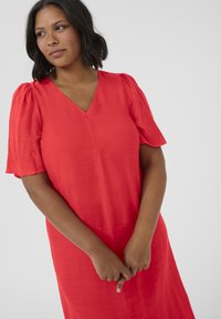 Abito rosso con scollo a V, maniche a sbuffo corte e una vestibilità rilassata. Tessuto morbido con una legggera lucentezza.