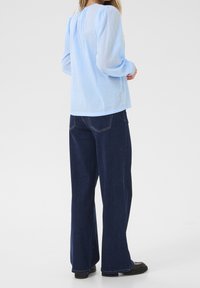 Vaaleansininen pusero, jossa on pussihihat ja teksturoidut pilkut, yhdistettynä tummansinisiin leveälahkeisiin farkkuihin ja mustiin platform-kengissä.