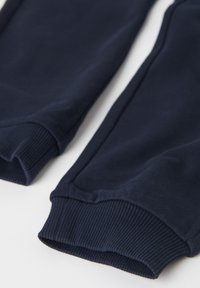 Marineblaue Jogginghose mit gerippten Bündchen, die eine weiche Textur und eine lockere Passform aufweist, auf weißem Hintergrund flach ausgelegt.