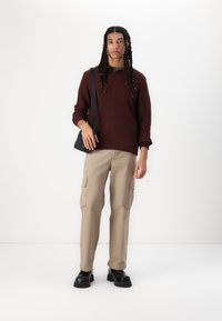 Bordeaux ribbet trøje, beige cargo bukser med sidelommer og sorte chunky-sål sko; model som bærer en lille sort crossbody taske.