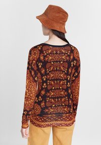 Camiseta de manga larga de punto con un patrón floral y de cachemira multicolor en tonos de naranja, negro y amarillo, con un cuello redondo.